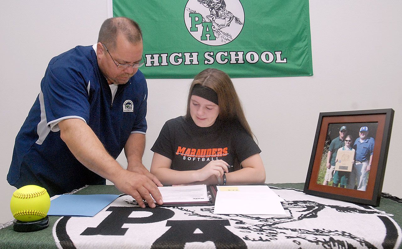 Keith Thorpe/Peninsula Daily News Port Angeles High School senior Lauren Lunt, seated, goes over paperwork with athletic director Dwayne Johnson prior to Lunt’s signing of a letter of intent on Friday to attend University of Mary in Bismarck, N.D., on a softball scholarship. A portrait of her, her father, Jeff Lunt, and grandfather, Jim Lunt, was displayed on the table.