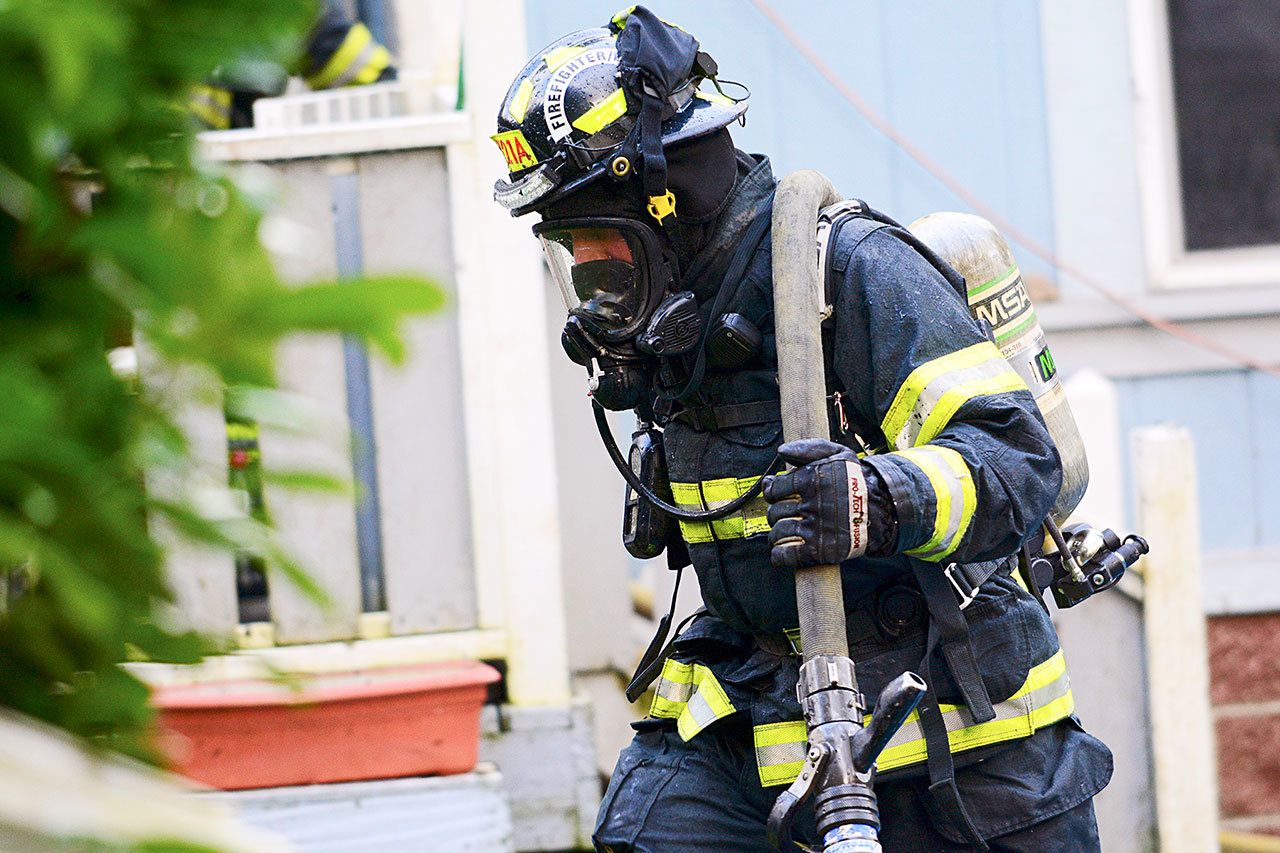 Firefighter Steven Bentley of Clallam County Fire District No. 2 carries a hose after responding to a fire at 833 Cottonwood Lane east of Port Angeles on Tuesday afternoon. (Jesse Major/Peninsula Daily News)