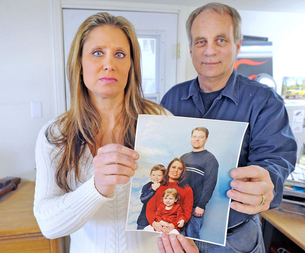 Joel Melom’s ex-wife Dana Linderman and stepfather Tim McCray pose with a photo of Melom with his family while he was still married to Linderman in Sedro-Woolley. Melom’s family is upset about a fake news story that was posted about the circumstances of his February 2016 death. (Scott Terrell/Skagit Valley Herald via AP)