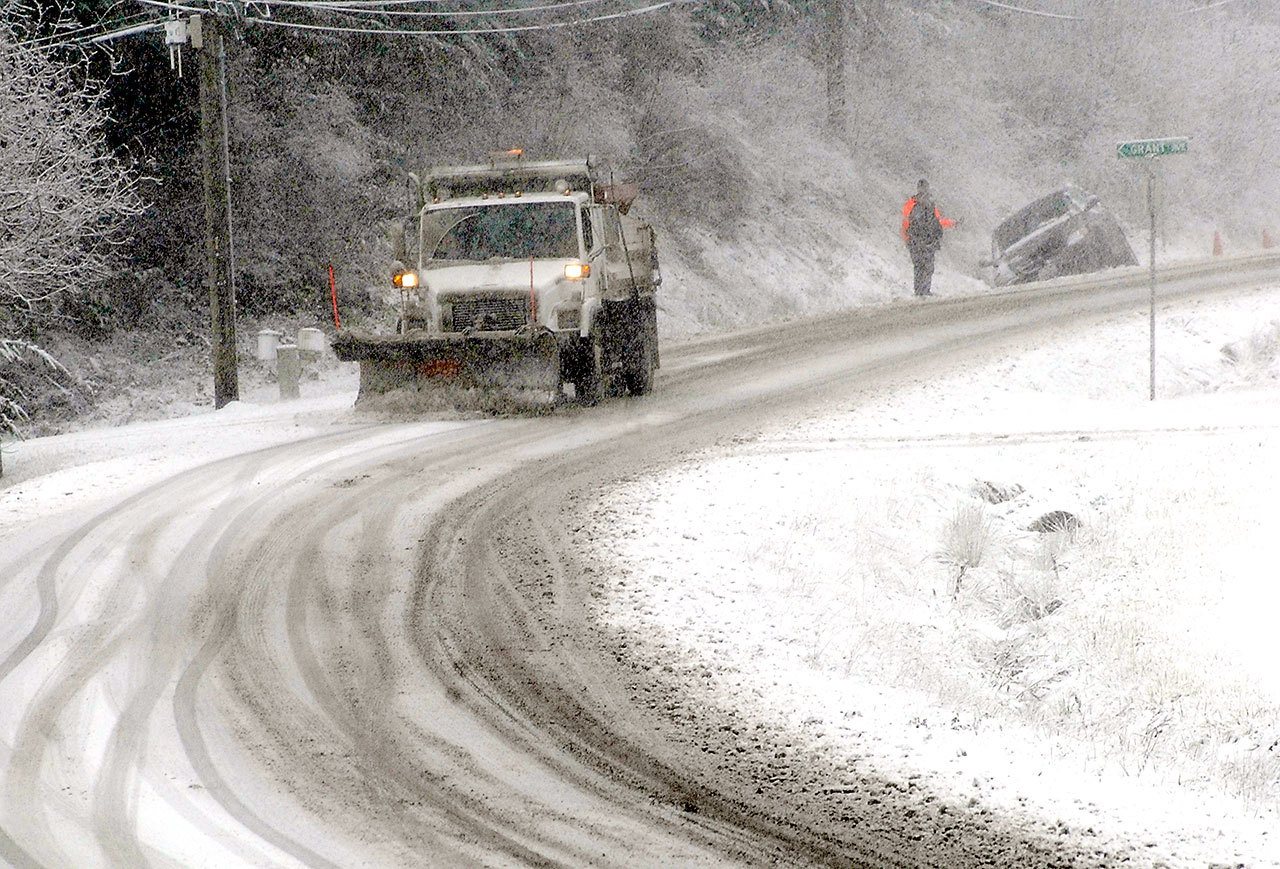 A snowplow clears slush from Mount Angeles Road near the Olympic National Park Visitor Center in Port Angeles as a vehicle sits in the ditch after sliding off the road Tuesday morning. (Keith Thorpe/Peninsula Daily News)