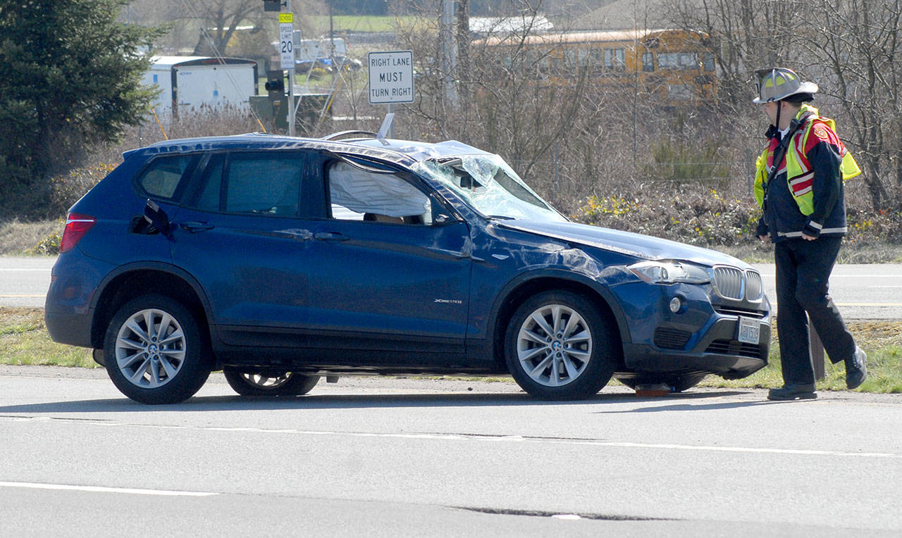 Clallam County Fire District No. 3 Chief Ben Andrews examines a car involved in a two-vehicle rollover collision on U.S. Highway 101 at Old Olympic Highway on Thursday that resulted in minor injuries to its occupants. (Keith Thorpe/Peninsula Daily News)