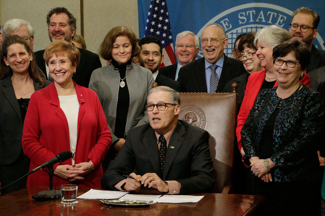 Gov. Jay Inslee is joined by lawmakers Wednesday in Olympia before signing a measure delaying a deadline for a reduction in the amount of money school districts can collect through local property tax levies. (Rachel La Corte/The Associated Press)