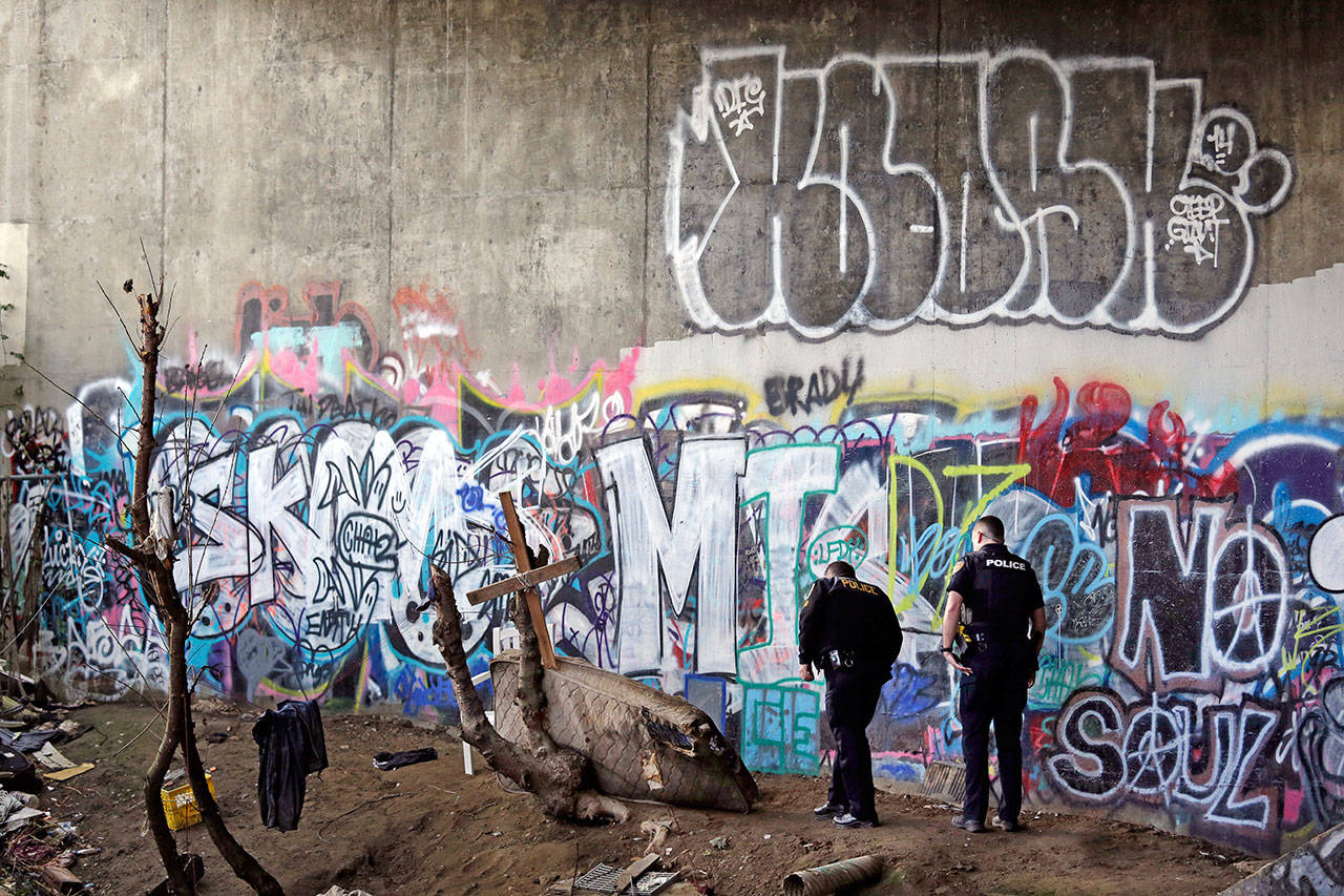 Police Sgt. Mike Braley, left, and officer Kevin Davis walk along the bottom of a highway overpass, a known location for drug use, to check for anyone living there in Everett last month. (Elaine Thompson/The Associated Press)