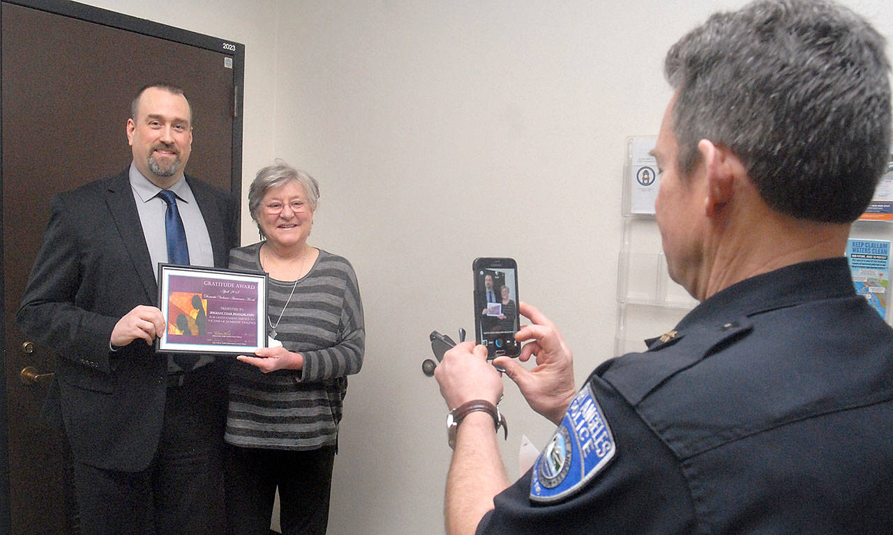 Port Angeles Police Chief Brian Smith, right, takes a photograph of Edward Bluhm, an investigator with U.S. Homeland Security, left, and Becca Korby, executive director of Healthy Families of Clallam County, after Bluhm was presented with an award of appreciation by Korby during Tuesday’s Clallam County commissioners meeting in Port Angeles. (Keith Thorpe/Peninsula Daily News)