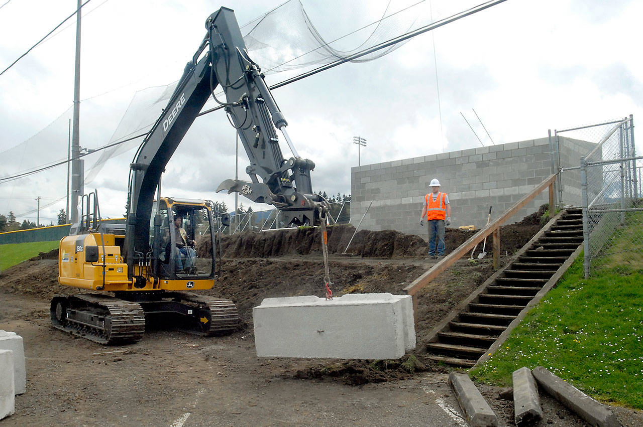 Port Angeles Lefties co-owner Jake Oppelt, right, watches as a loader operated by Jamey Watts of Lakeside Industries hoists a concrete retaining block into place behind a new home team dugout at Port Angeles Civic Field on Saturday. Lakeside contributed the use of its employees and equipment to help with modifications to the field to accommodate the start of West Coast League baseball on June 1. (Keith Thorpe/Peninsula Daily News)