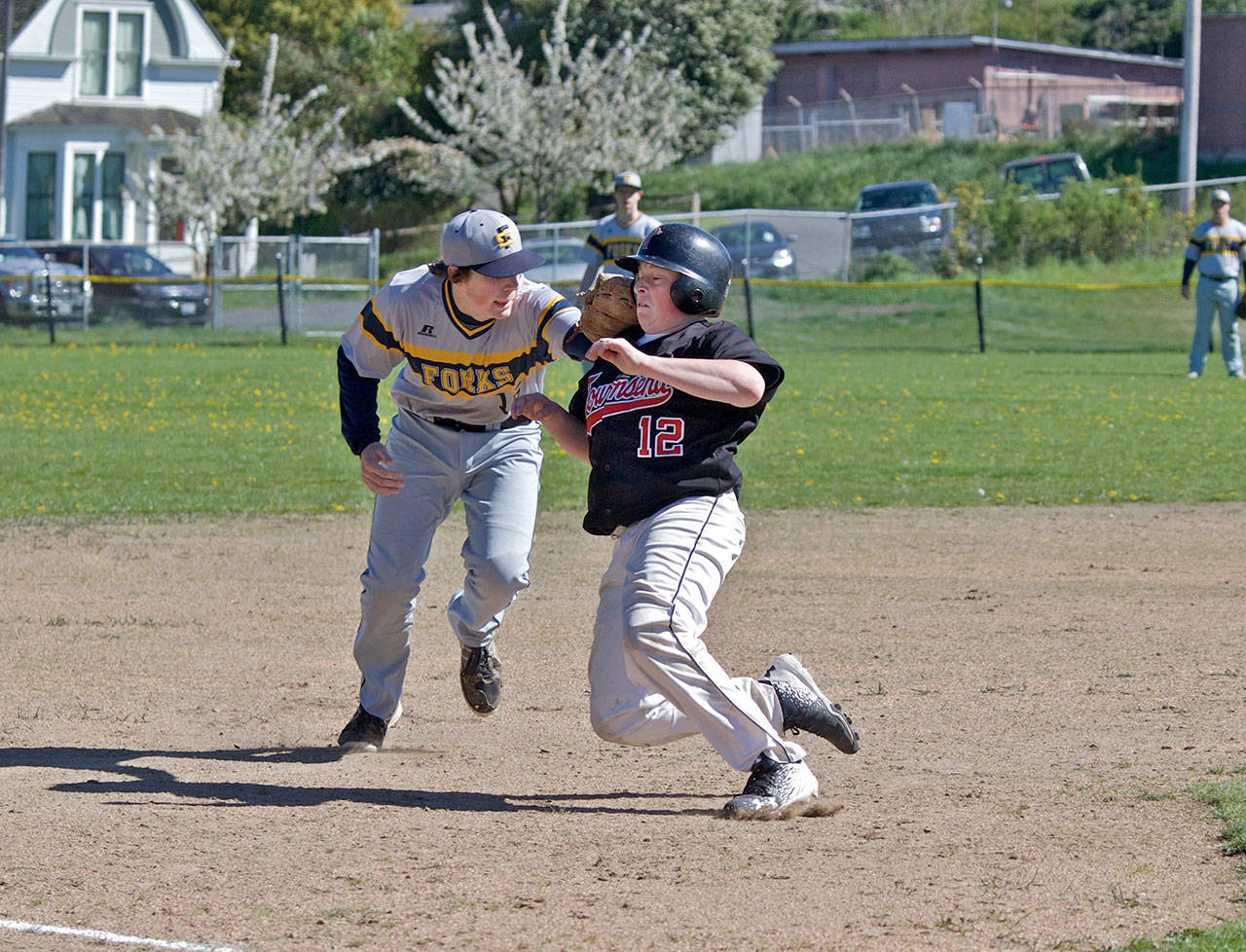 Steve Mullensky/for Peninsula Daily News Port Townsend’s Travis McComaghy takes it on the chin as he’s tagged out by Forks’ third baseman, Billy Palmer, during a game in Port Townsend on Monday.