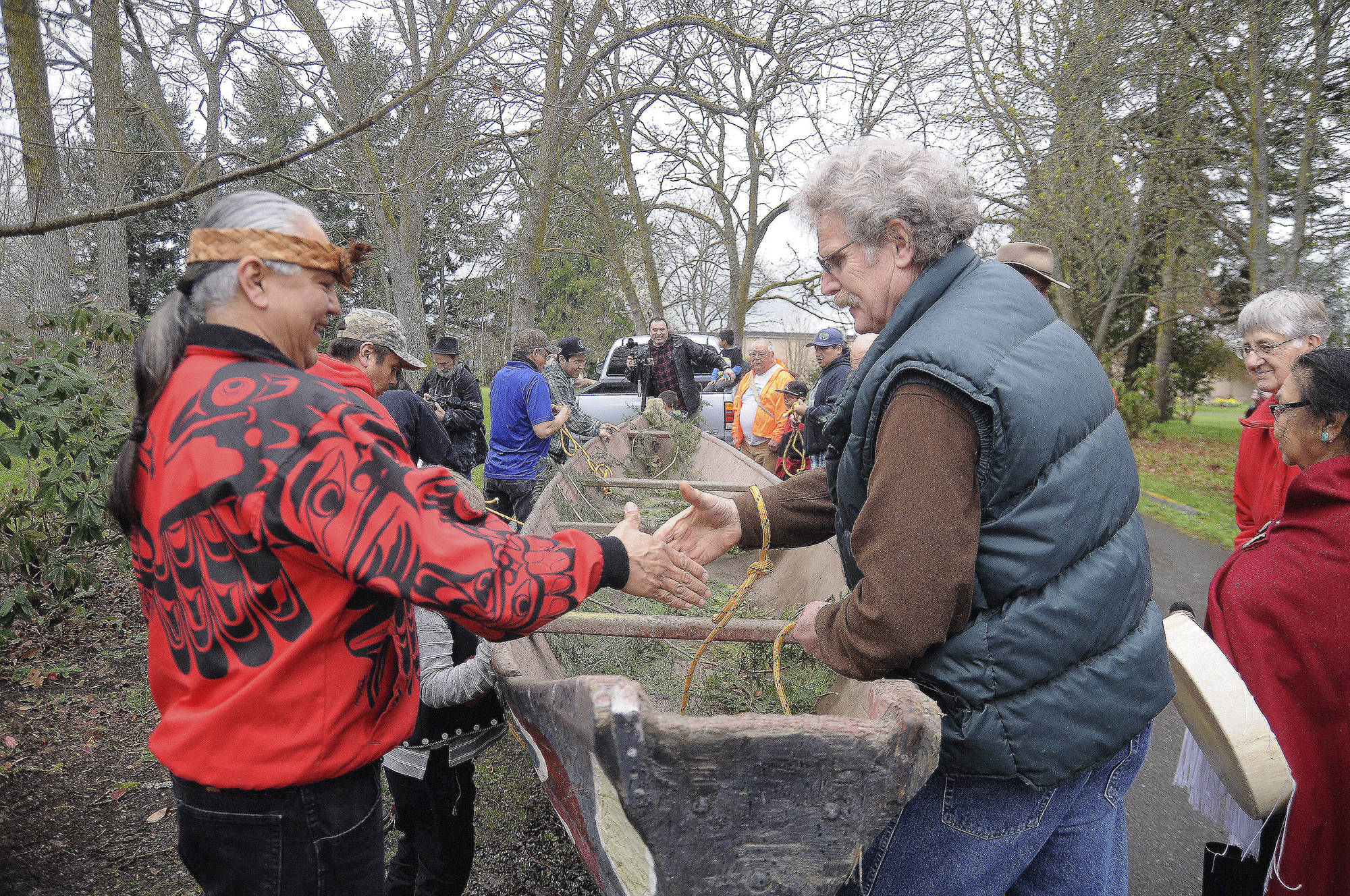 Vince Penn of the Quileute Tribe, left, and Frank Hanson, education and outreach coordinator at the University of Washington’s Olympic Natural Resources Center, shake hands as a handmade canoe carved by William E. Penn is removed from Pioneer Memorial Park on April 8. (Michael Dashiell/Olympic Peninsula News Group)