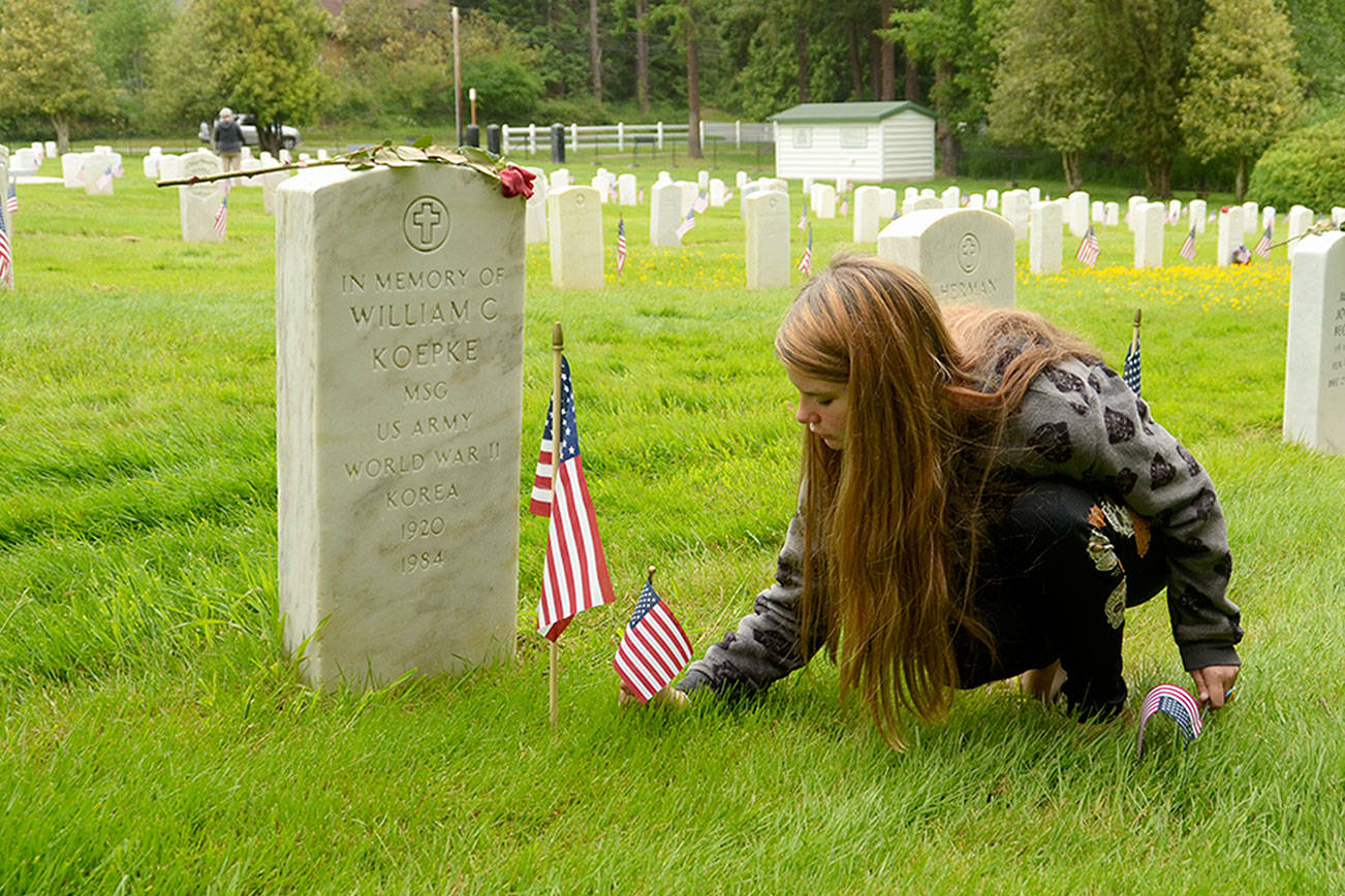 Oracle Holms of Port Hadlock places flags at the gravestones of veterans in the cemetery at Fort Worden on Monday. (Cydney McFarland/Peninsula Daily News)