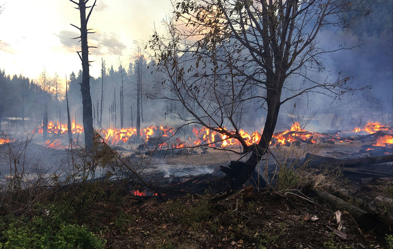 In this Tuesday photo provided by Chelan County Fire District 3, logs burn near Leavenworth. The wildfire that started at an old log-storage site has prompted evacuation orders for homes and cabins at a popular Washington state hiking and skiing destination, officials said Wednesday. (Ben Torkelson/Chelan County Fire District 3 via AP)