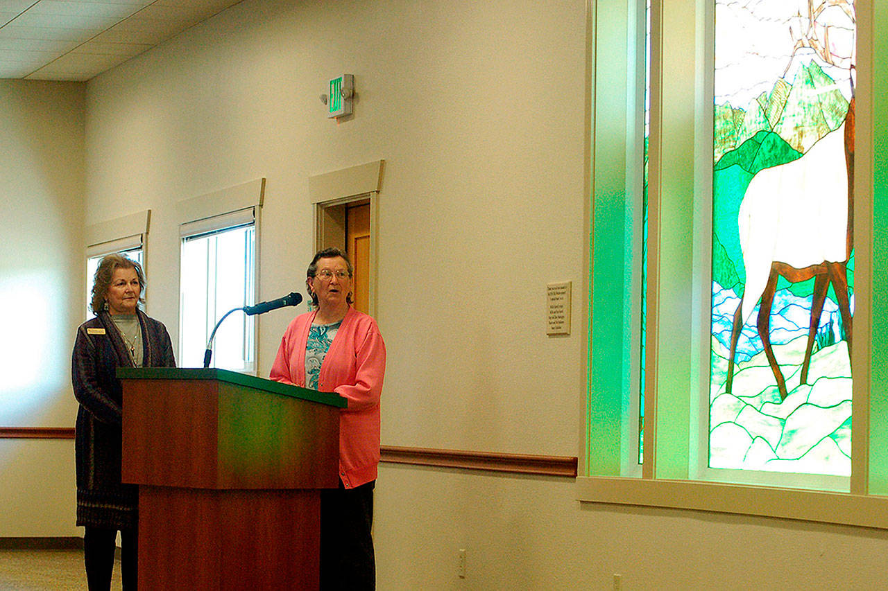 Millie Harrell, on right, created and donated the glass elk to the City of Sequim for its Guy Cole Convention Center remodel. She told a crowd May 16, including Sharon DelaBarre, chairman of the Sequim Arts Advisory Commission, on left, that she wanted it to stay in Sequim. (Matthew Nash/Olympic Peninsula News Group)