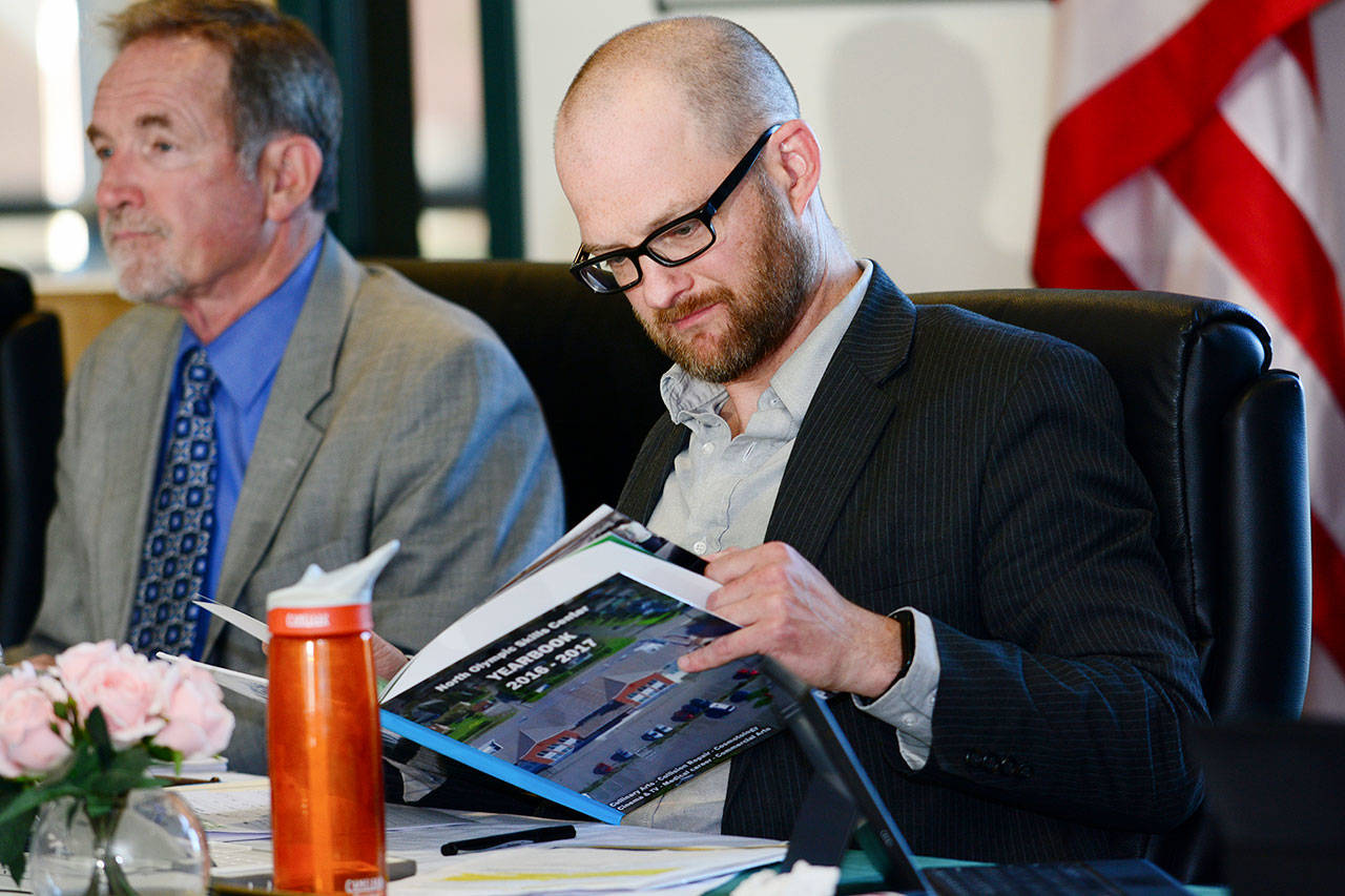 Port Angeles School Board President Joshua Jones reads through the first and last yearbook for the North Olympic Peninsula Skills Center during a school board meeting Thursday. (Jesse Major/Peninsula Daily News)