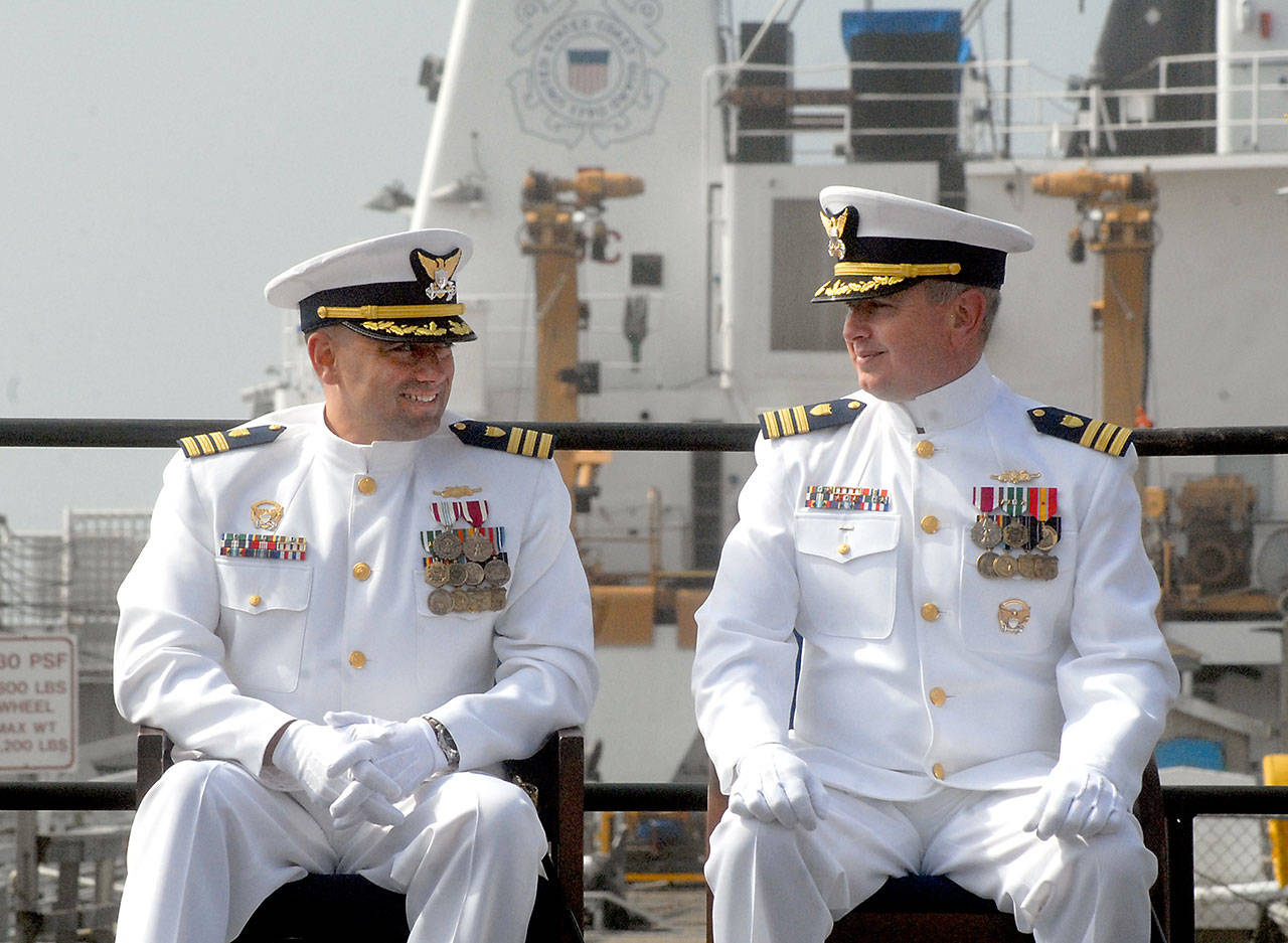 U.S. Coast Guard Cmdr. Benjamin Berg, left, and Cmdr. Christofer German share a moment of levity during a ceremony Friday shifting command of the cutter Active, in the background, from Berg to German at Air Station/Sector Field Office Port Angeles. (Keith Thorpe/Peninsula Daily News)