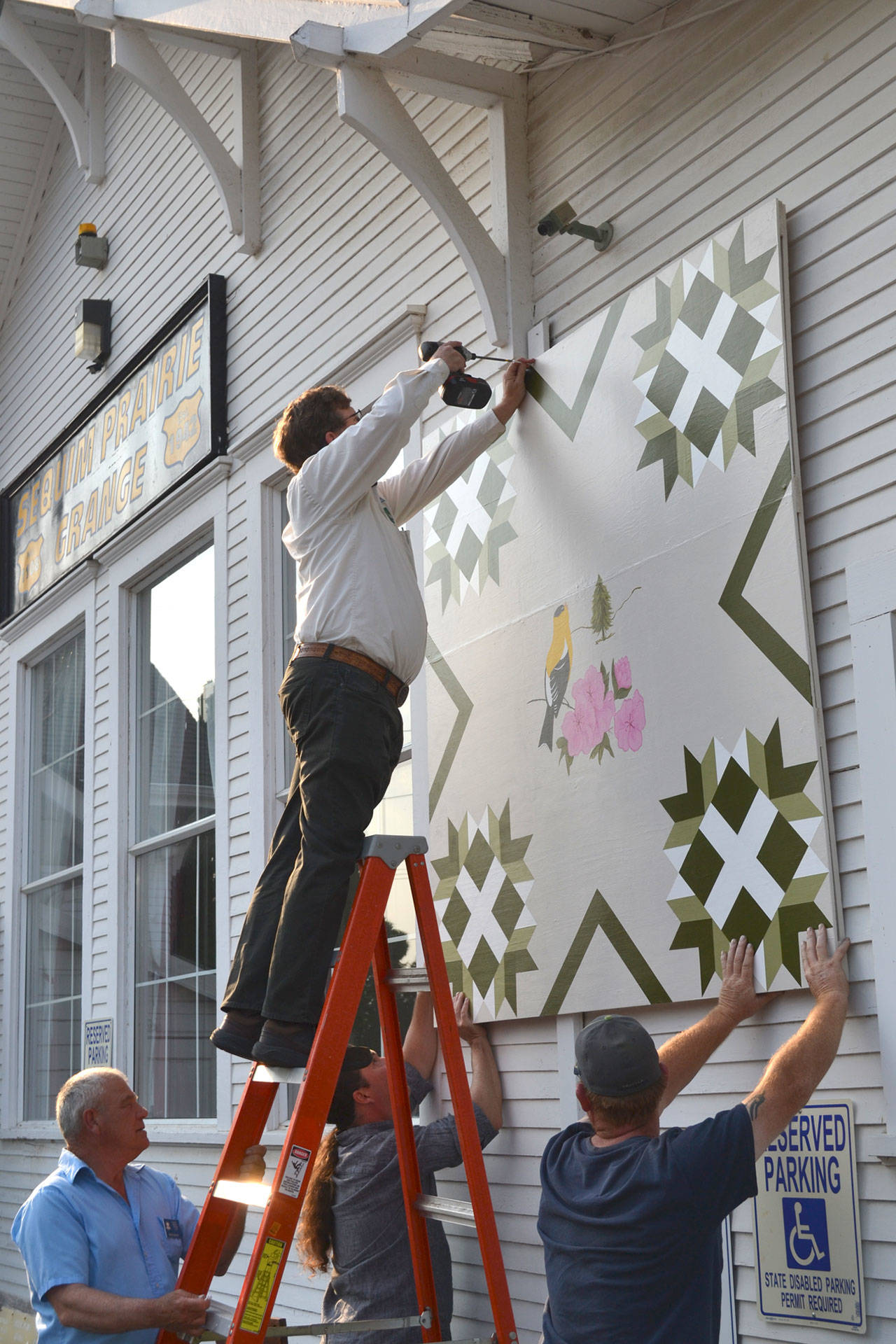 Volunteers attach a 6-foot by 6-foot Barn Quilt on Aug. 12, 2015, on the side of Macleay Hall as part of the Washington State Heritage Quilt Trail. It’s one of 16 quilts on display in Washington. Sequim Gazette file photo by Matthew Nash