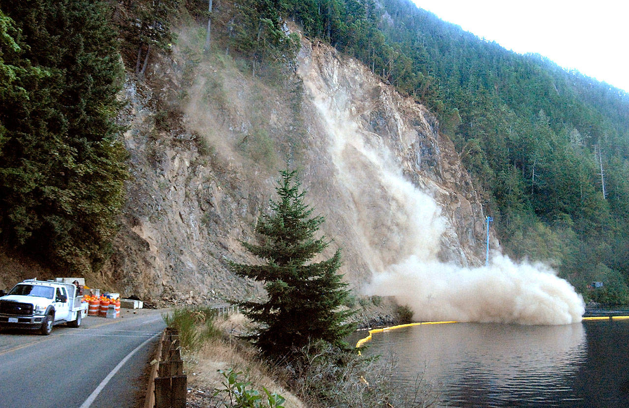 A plume of dust floats across U.S. Highway 101 and over the surface of Lake Crescent after workers pry loose a large boulder during rock scaling near Barnes Point on Wednesday. (Keith Thorpe/Peninsula Daily News)