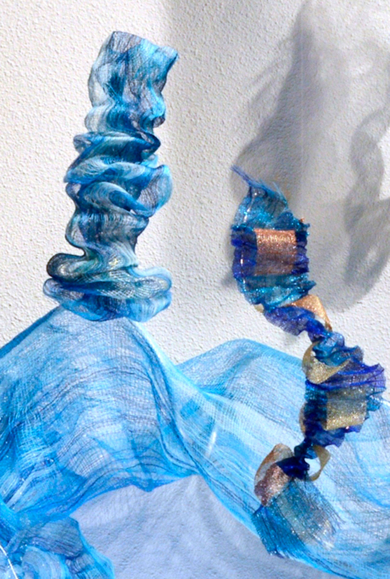 Cathie Wier’s “Turbulence” is a handwoven installation done on a 4- shaft loom using stainless steel thread, copper thread, monofilament, polyester thread and armature wire in a technique called “doubleweave.” Her inspiration is the wild rivers of the Olympics. In the smooth flowing eddies she sees subtle evidence of the tidepools that develop and flow by.