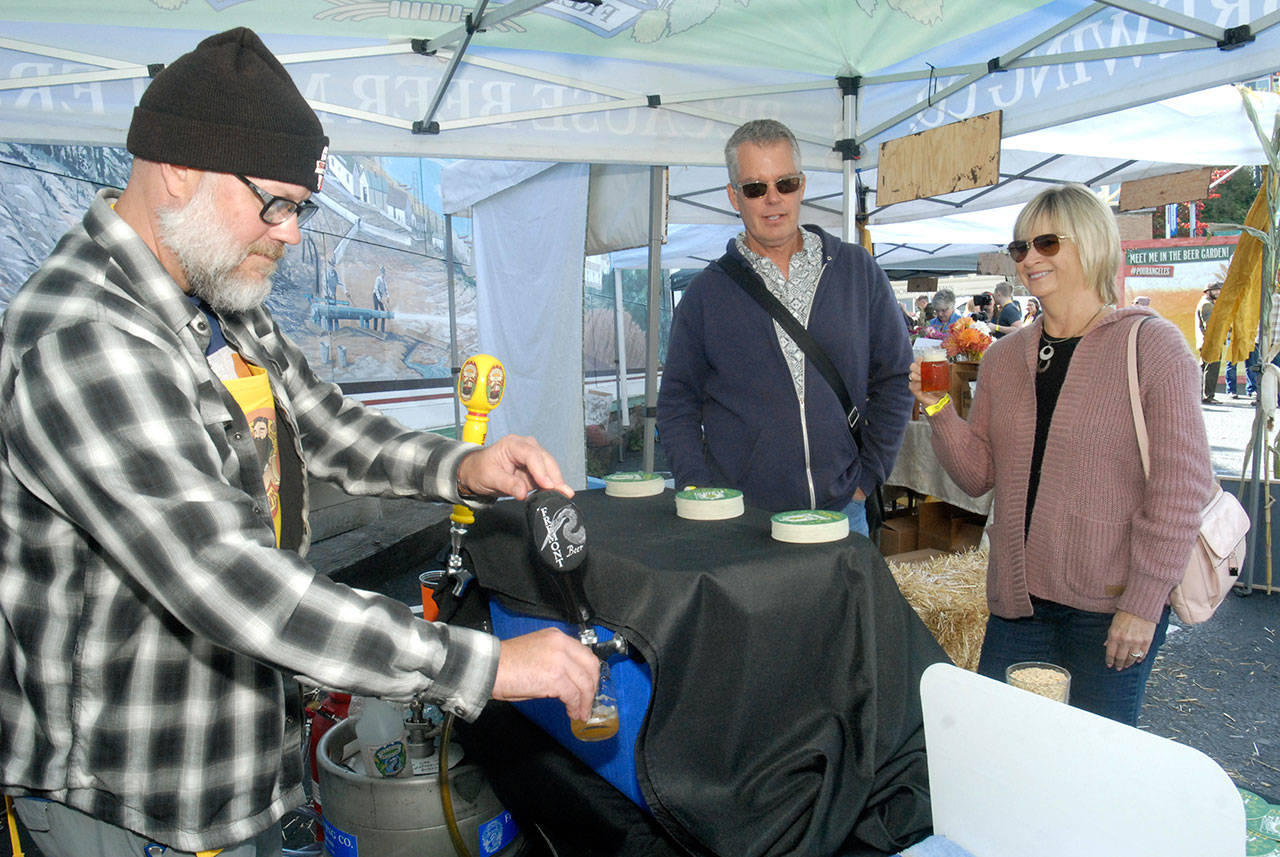 Erik Good of Port Angeles, representing Seattle-based Fremont Brewing, left, pours a beer sample for Jim and Ann Jensen of Sequim at the second annual Arts Draughts Festival, a celebration of beer, wine and cider, along with music and a craft fair, in 2016 in downtown Port Angeles. (Keith Thorpe/Peninsula Daily News)