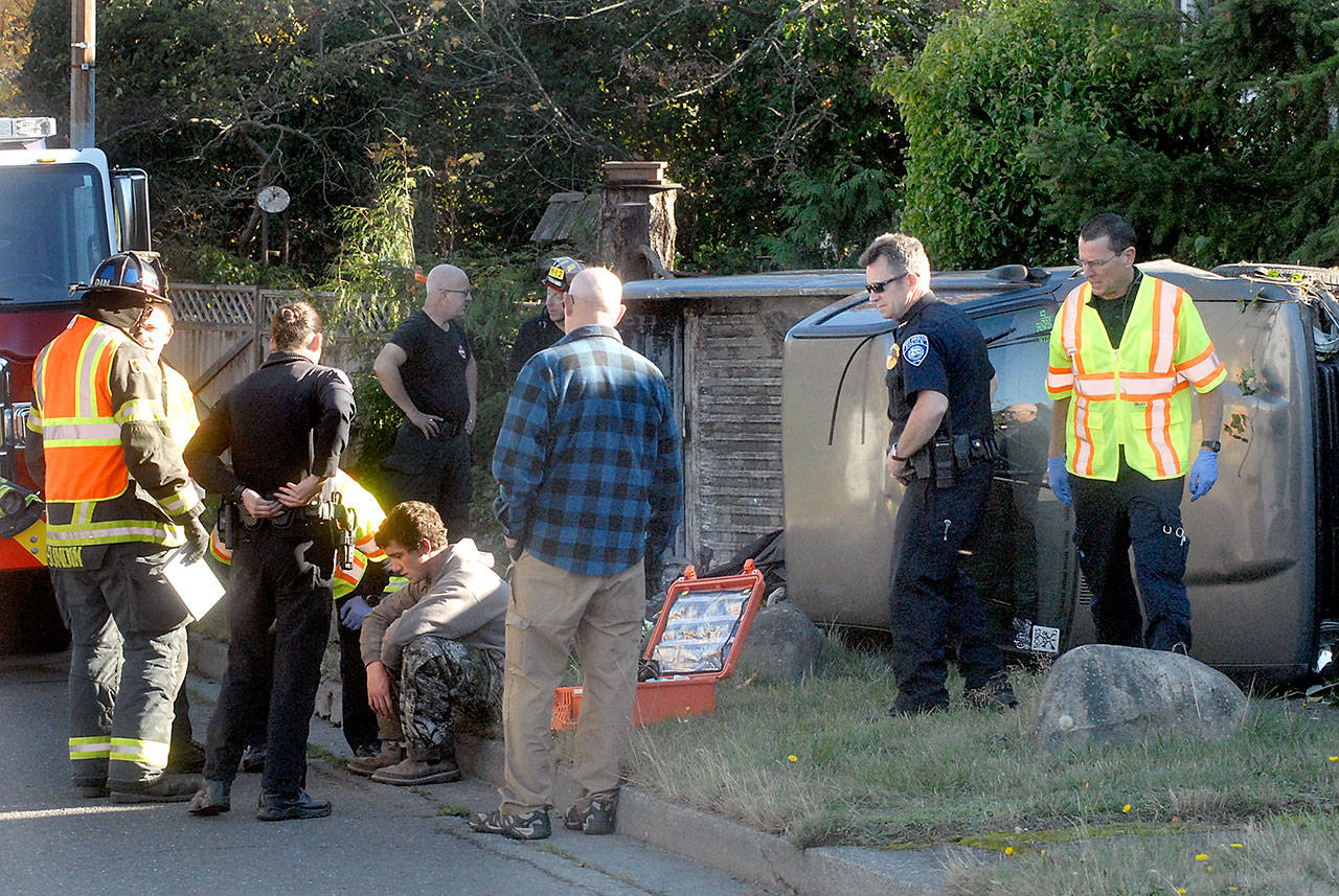 Police and rescue workers gather around the occupant of a pickup truck involved in a rollover near the curve at Tumwater and Fifth streets in Port Angeles on Friday. (Keith Thorpe/Peninsula Daily News)