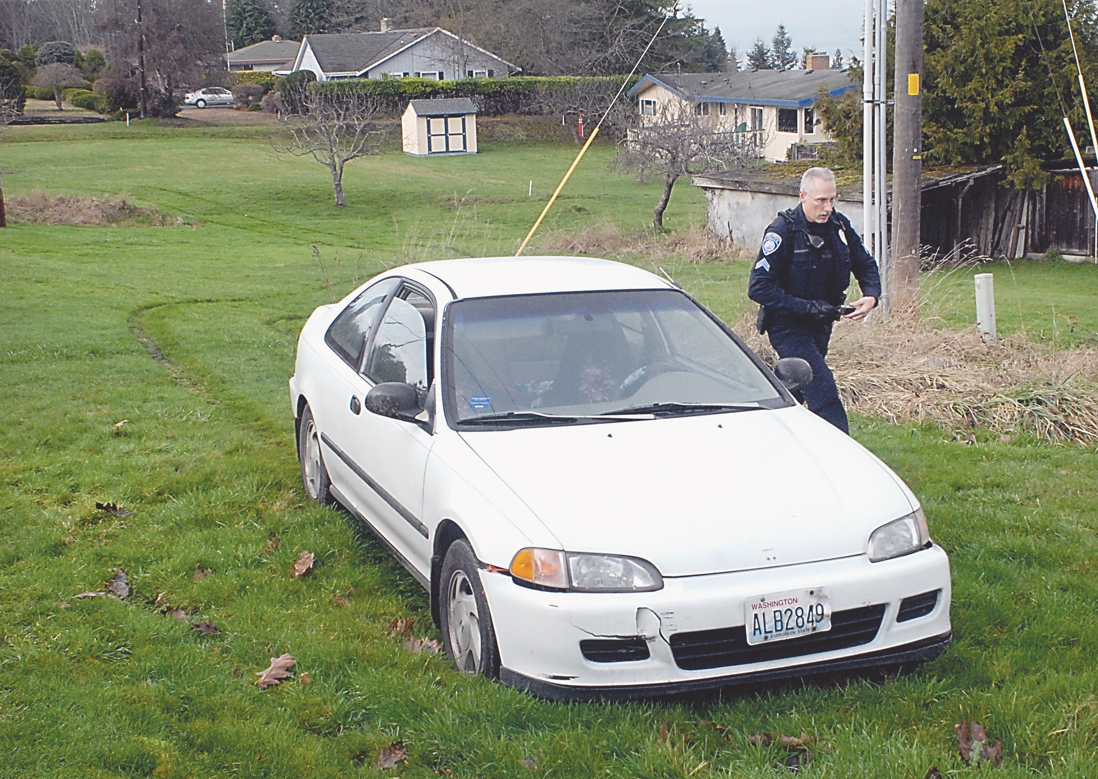 Port Angeles Police Officer David Drombowski examines a car that was driven through backyards and then abandoned behind 1723 Lambert Lane after a short chase in Port Angeles. (Keith Thorpe/Peninsula Daily News)