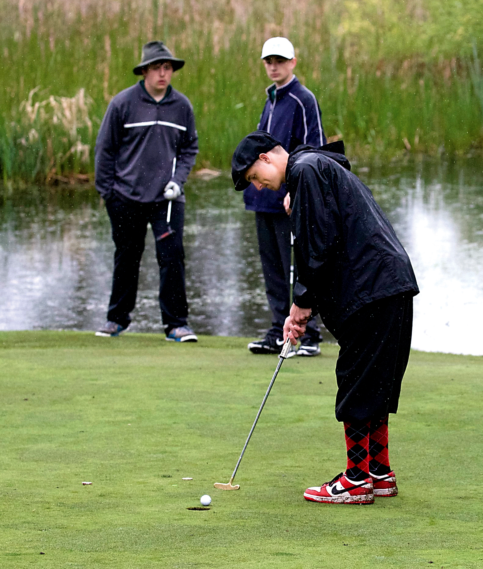 Port Angeles' Logan Kovalenko and Mathew Locke watch as Port Townsend's Jacob Ralls sinks a putt at Port Townsend Golf Course. (Steve Mullensky/for Peninsula Daily News)