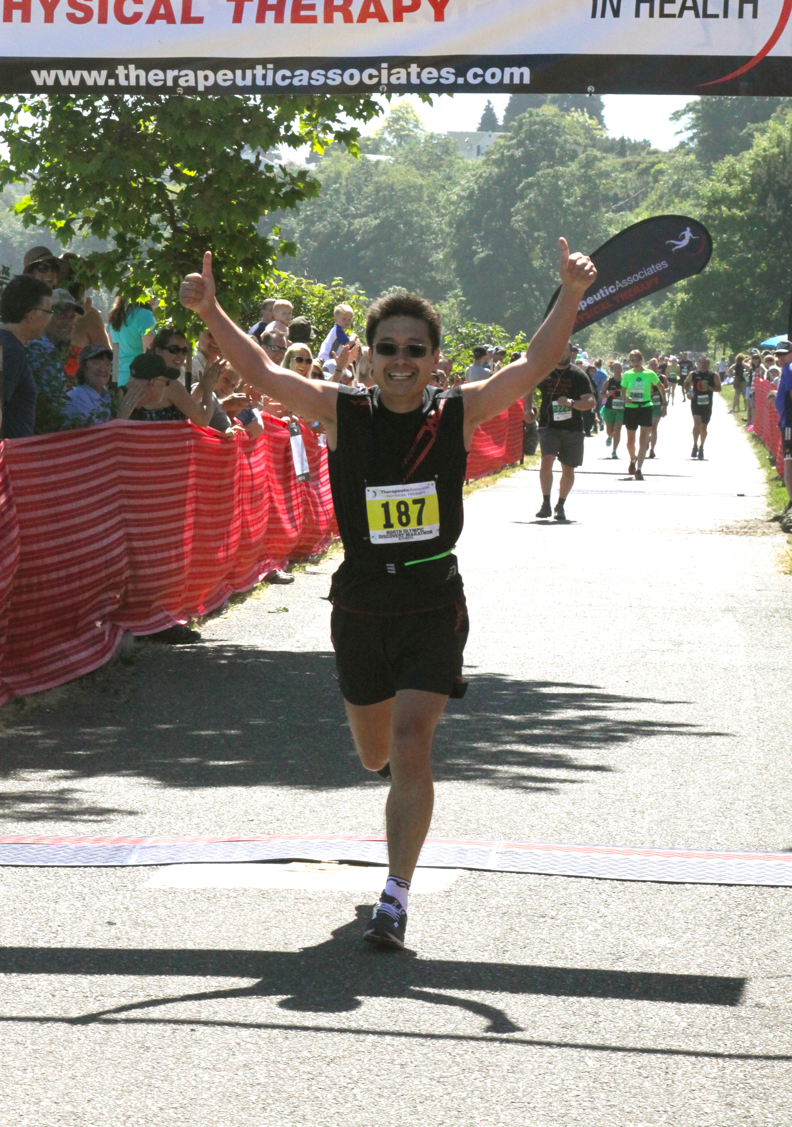 Marathon winner Yusheng Ni puts two thumbs in the air as he crosses the finish line. (Dave Logan/for Peninsula Daily News)