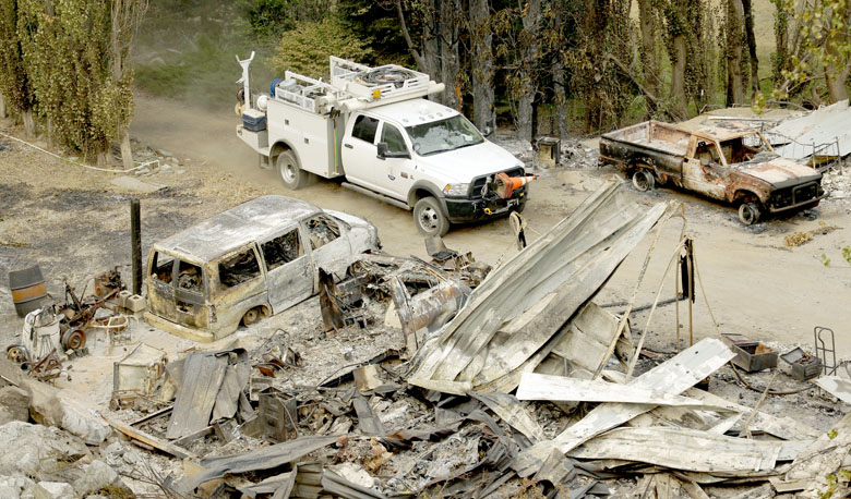 A Chelan County Public Utility District truck drives near a burned structure Monday outside Chelan. The Associated Press