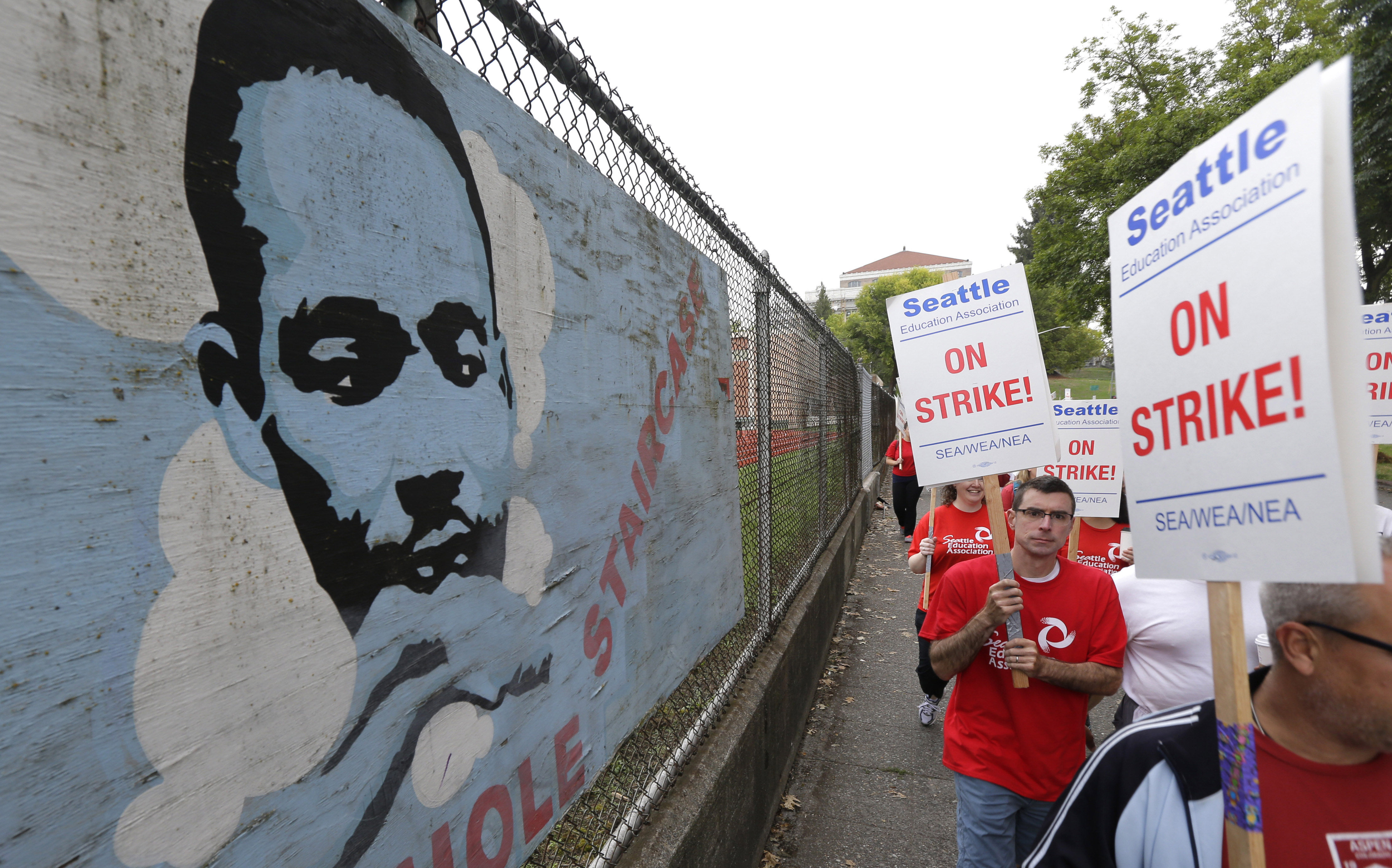 Striking Seattle School District teachers and other educators walk a picket line past an image of Martin Luther King Jr.