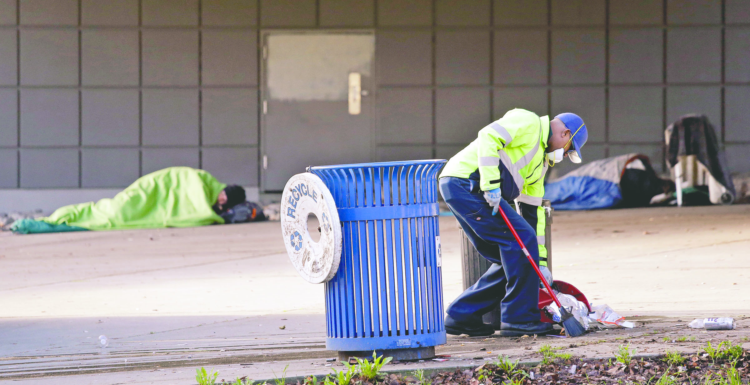 A contract worker cleans up trash Tuesday as men continue to sleep behind him under a Seattle overpass near where police arrested three teenage boys. — The Associated Press ()