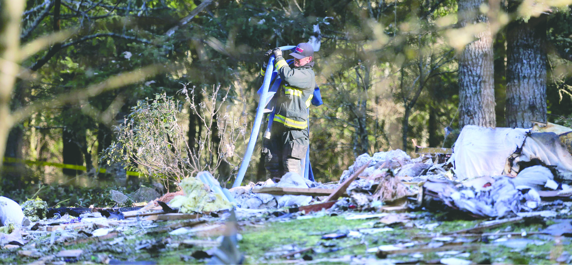 A South Kitsap Fire and Rescue firefighter collects a hose at the site of a home explosion in the 3800 block of Soholt Lane in Port Orchard on Tuesday. The remains of two people were found following a powerful explosion that morning that leveled a home in Western Washington. — Larry Steagall/Kitsap Sun via AP ()