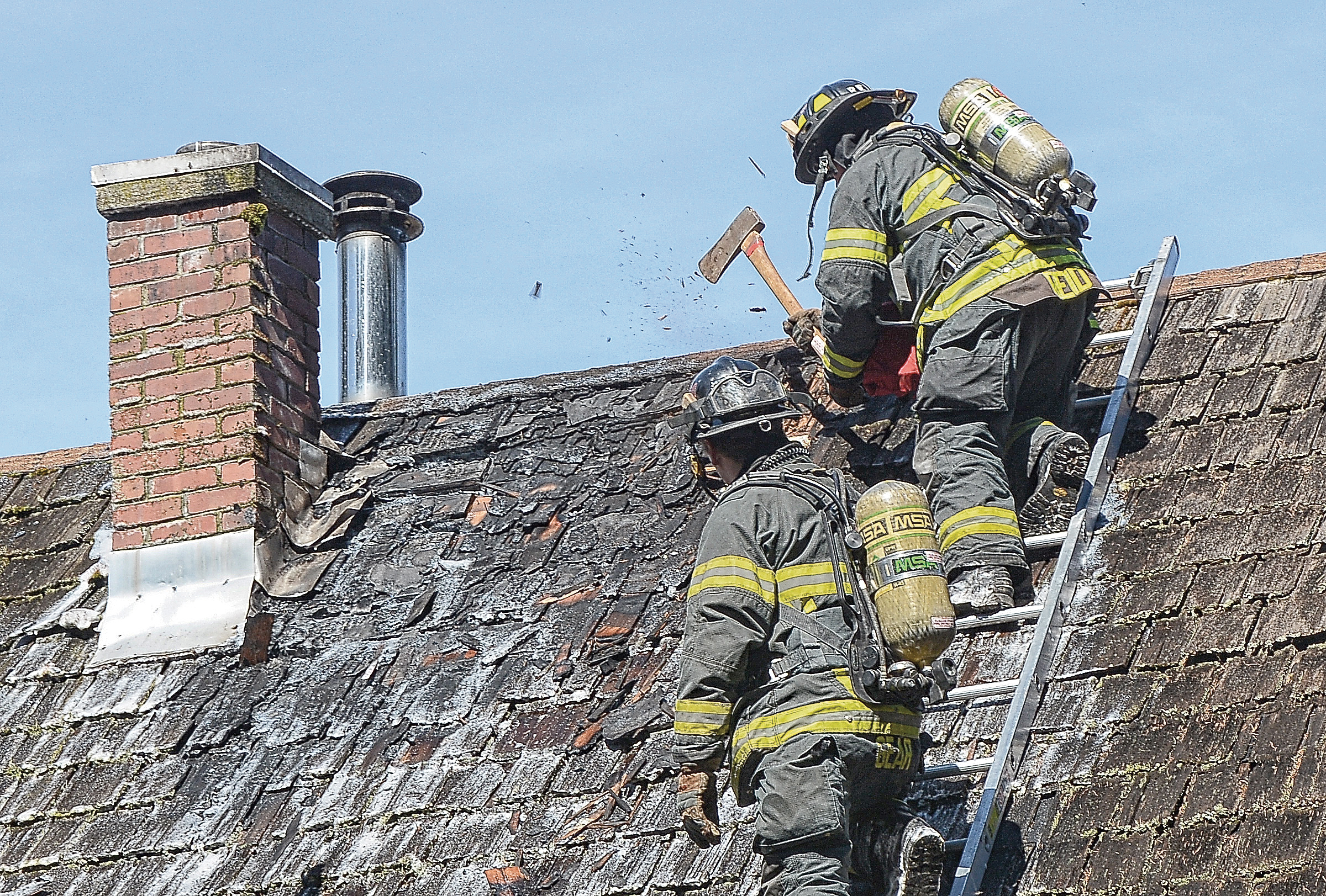 Clallam County Fire District No. 2 firefighters crawl onto a smoldering roof at 73 Gakin Road west of Port Angeles on Tuesday. — Jay Cline/Clallam County Fire District No. 2 ()