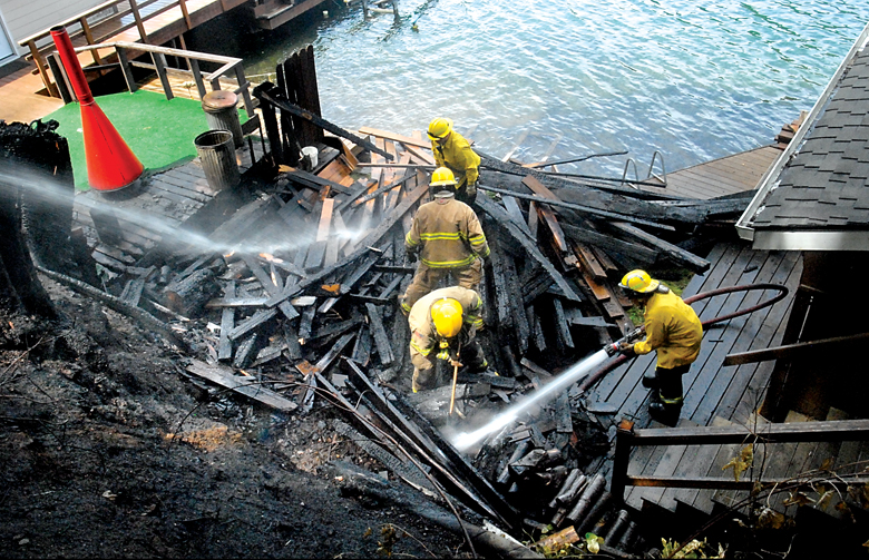 Firefighters from Clallam County Fire District No. 2 look for hot spots after a fire heavily damaged a dock and scorched an adjoining hillside at 880 S. Shore Road at Lake Sutherland on Tuesday. (Keith Thorpe/Peninsula Daily News)
