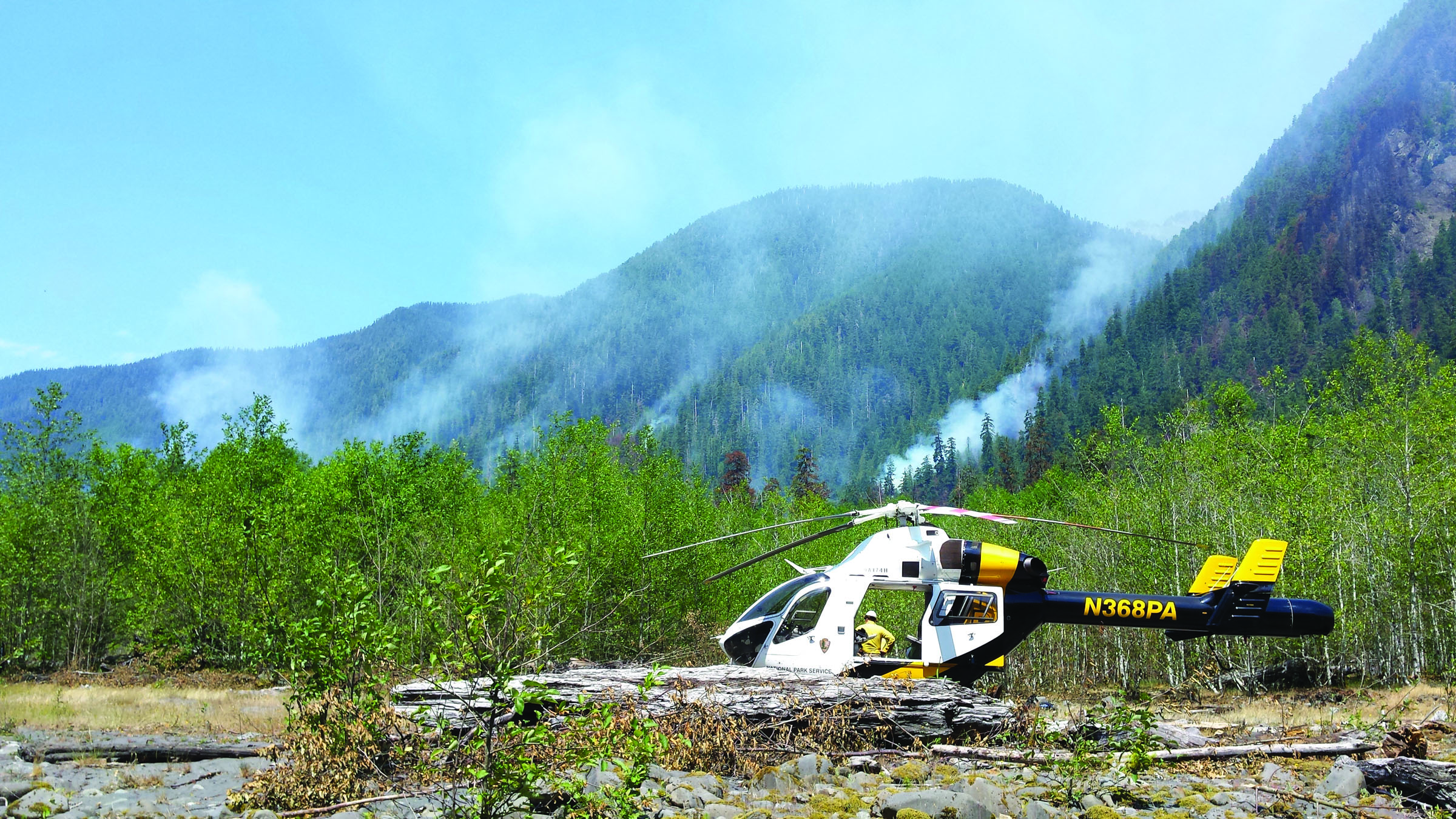 A helicopter stands ready to aid in fighting the Paradise Fire as smoke from the blaze in the Queets Rain Forest rises in the distance. — U.S. Forest Service ()