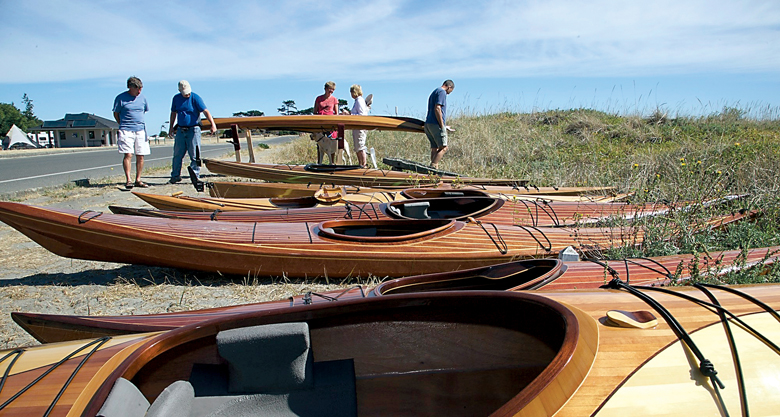 Kayak enthusiasts examine a custom-built wooden kayak amid many lined up during the 17th annual West Coast Wooden Kayak Rendezvous under sunny skies at Fort Worden State Park on Saturday. The gathering continues today. Steve Mullensky/for Peninsula Daily News