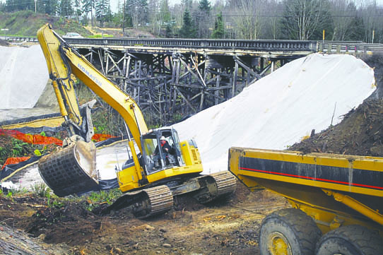 The wooden bridge over McDonald Creek carries cars on U.S. Highway 101 west of Sequim as an excavator moves earth in the foreground. Keith Thorpe/Peninsula Daily News