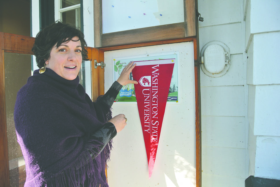 Washington State University's Jefferson County Extension Director Laura Lewis hangs a school banner at Cupola House in Port Townsend. Charlie Bermant/Peninsula Daily News