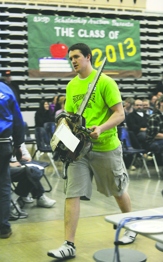 Forks High School senior Nate Brock carries an antique chain saw that was auctioned over the weekend at the 49th Quillayute Valley Scholarship Auction. Lonnie Archibald/for Peninsula Daily News
