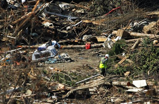 A search worker Tuesday walks near a camper shell in the debris from the deadly mudslide. The Associated Press