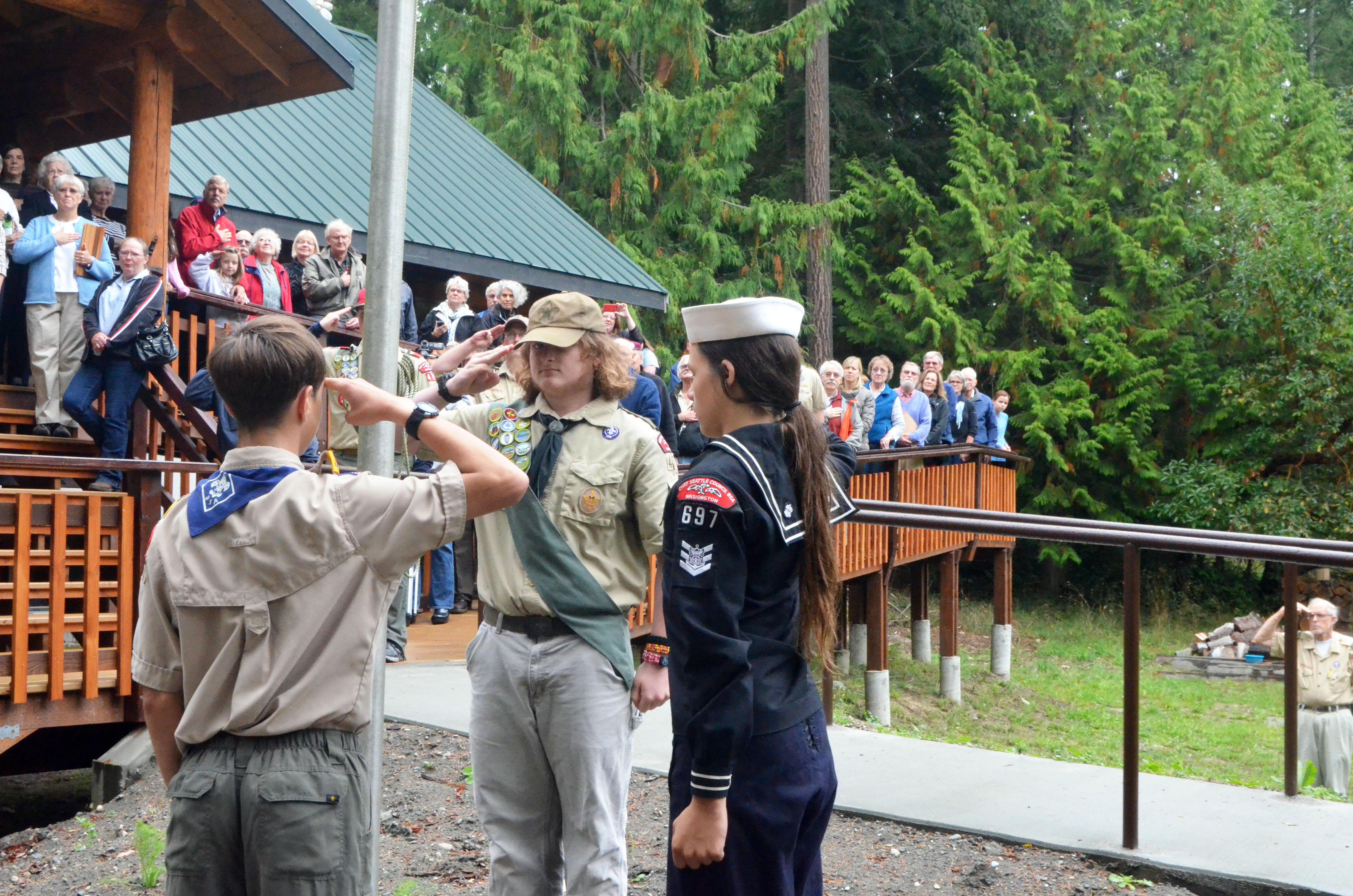 Boy Scouts Alex Brown and Wil Gale and Sea Scout Elijah Johnston lead about 100 people in the flag salute during Sunday's dedication of the Scout Cabin. Charlie Bermant/Peninsula Daily News