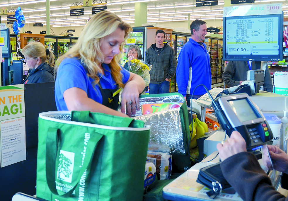 QFC checker Deb Boone places groceries in a reusable bag Thursday