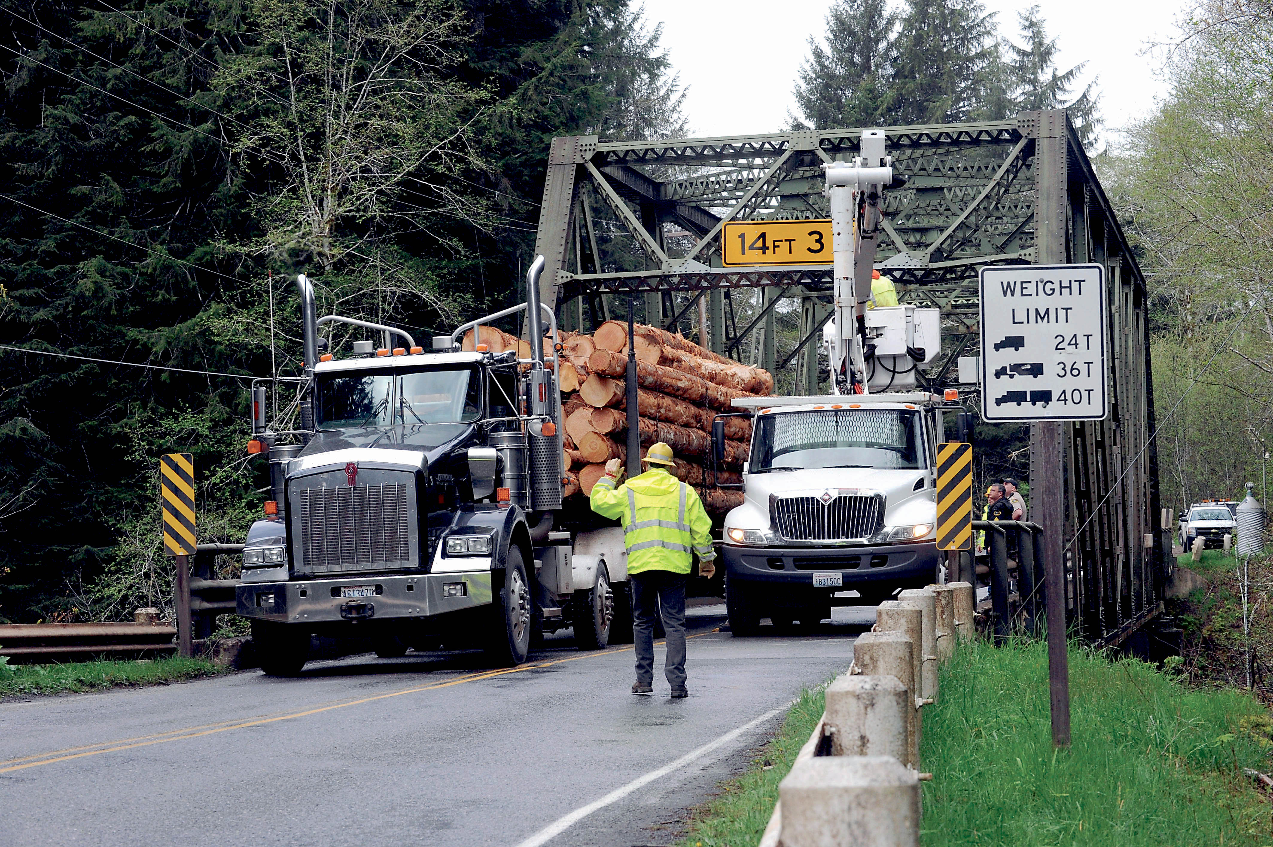 A Clallam County Road Department worker guides a log truck across the Sol Duc River bridge on Quillayute Airport Road on Tuesday as others repair the steel-truss structure. —Photo by Lonnie Archibald/for Peninsula Daily News