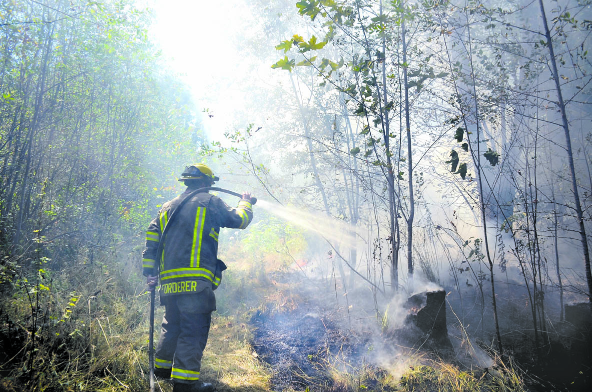 A firefighter sprays water on a small brush fire off South Bagley Creek Road on Tuesday. Patrick Young/Clallam County Fire District No. 3