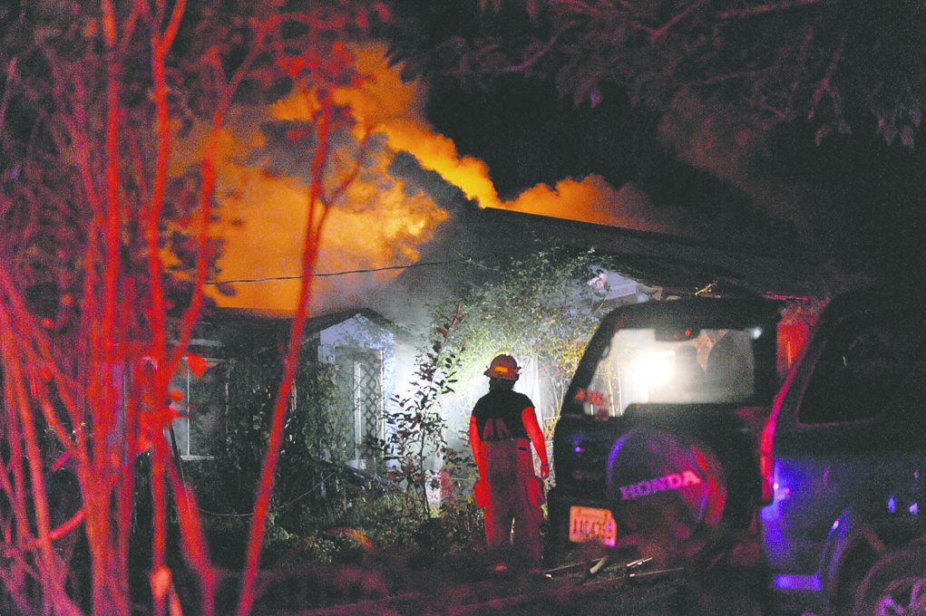 Smoke rising from a home on Tyee Ridge Road in Beaver is illuminated by the lights from fire trucks early Friday morning. Lonnie Archibald/for Peninsula Daily News