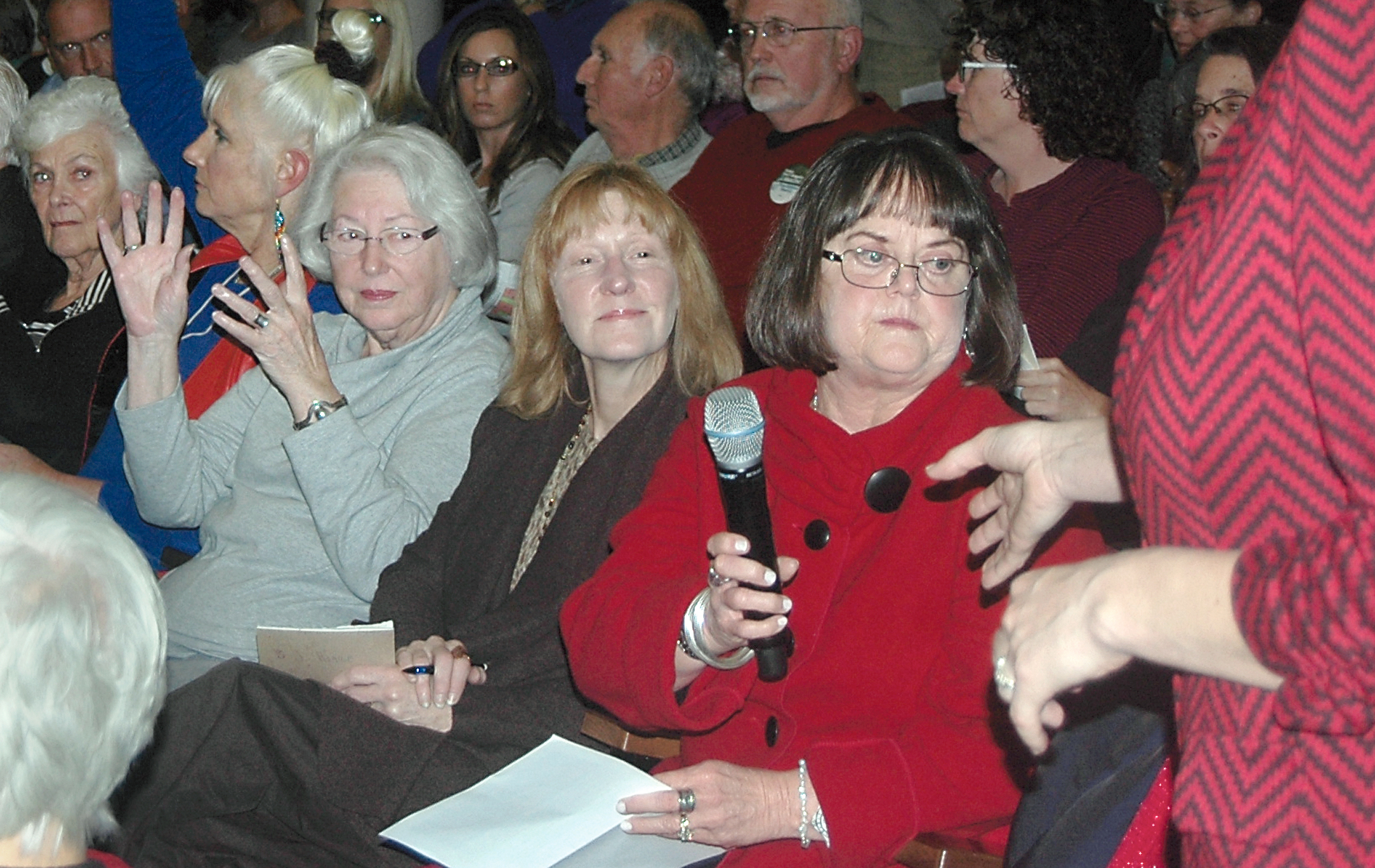 Fluoridation opponent Judi Hangartner of Port Angeles hands back a microphone at a fluoridation forum Thursday at Port Angeles City Hall while an onlooker silently signals her approval by fluttering her hands