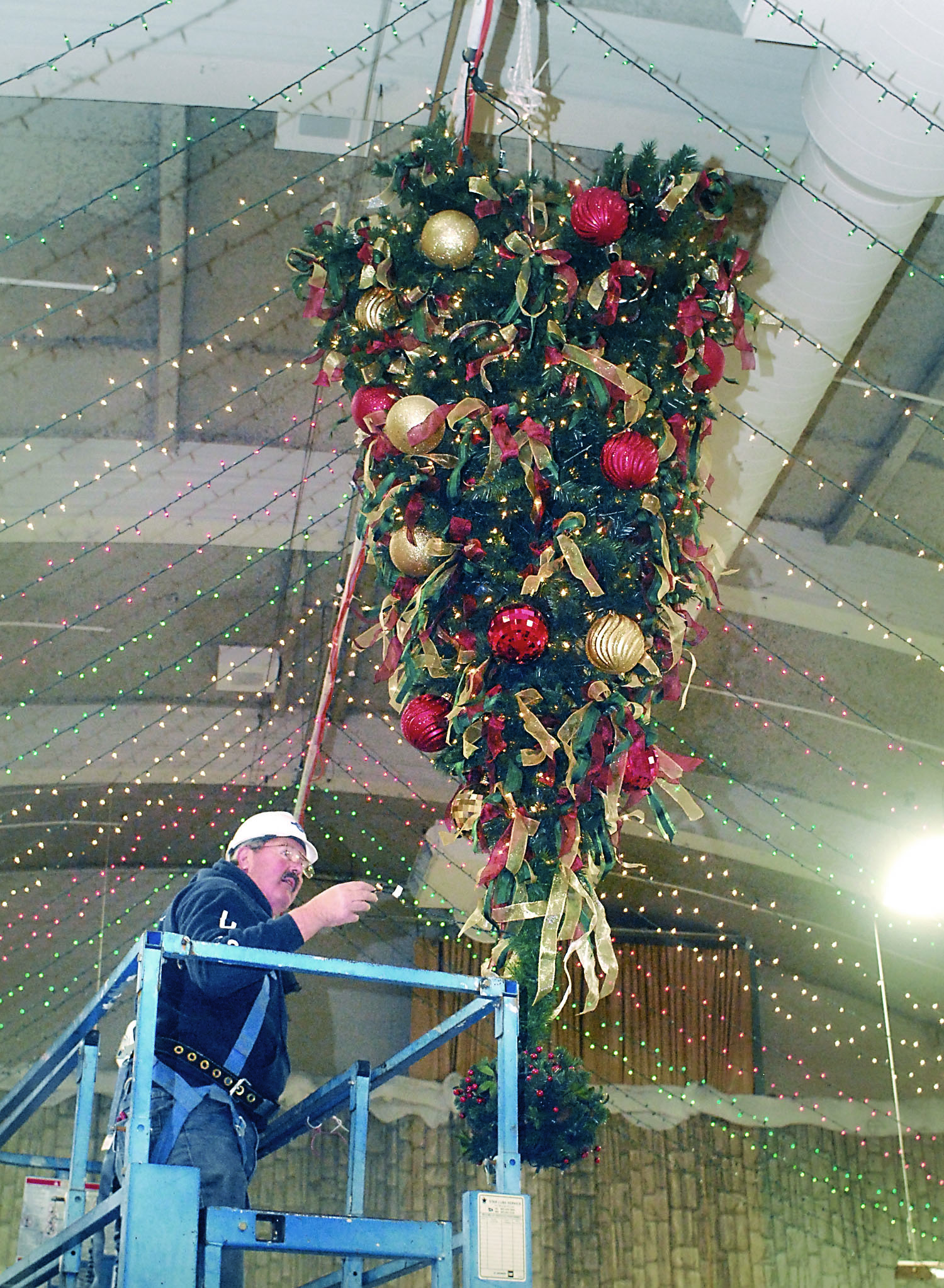 Harry Hebert works from a lift as he adds a string of lights Tuesda to a Christmas tree that hangs upside-down from the ceiling as part of the decorations at Vern Burton Community Center in Port Angeles. —Photo by Keith Thorpe/Peninsula Daily News