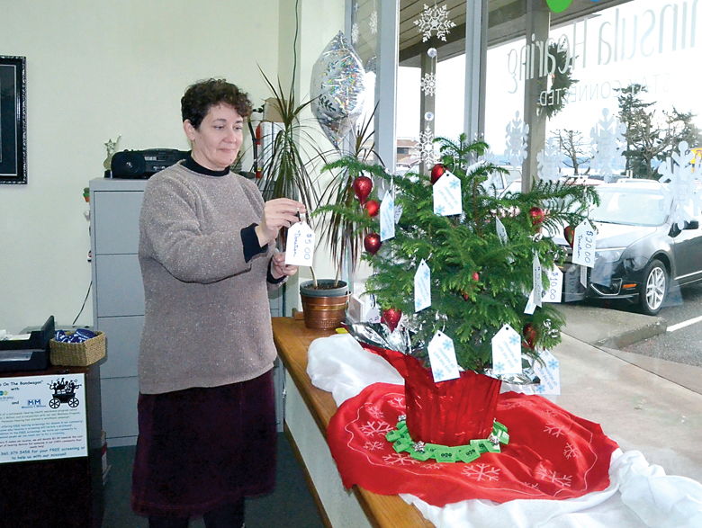 Peninsula Hearing specialist Elisa Welch posts a donation star on the shop’s Christmas tree. The center is raising money to subsidize distribution of hearing devices for people at or under the poverty line. — Charlie Bermant/Peninsula Daily News
