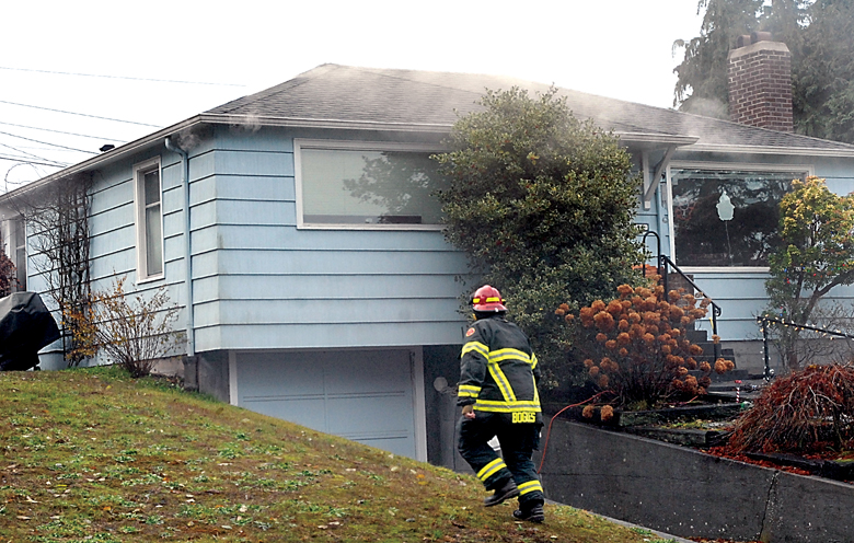Port Angeles Fire Capt. Keith Bogues approaches a house at 808 E. 10th St. in Port Angeles after smoke was reported coming from under the eaves on Friday morning. — Keith Thorpe/Peninsula Daily News
