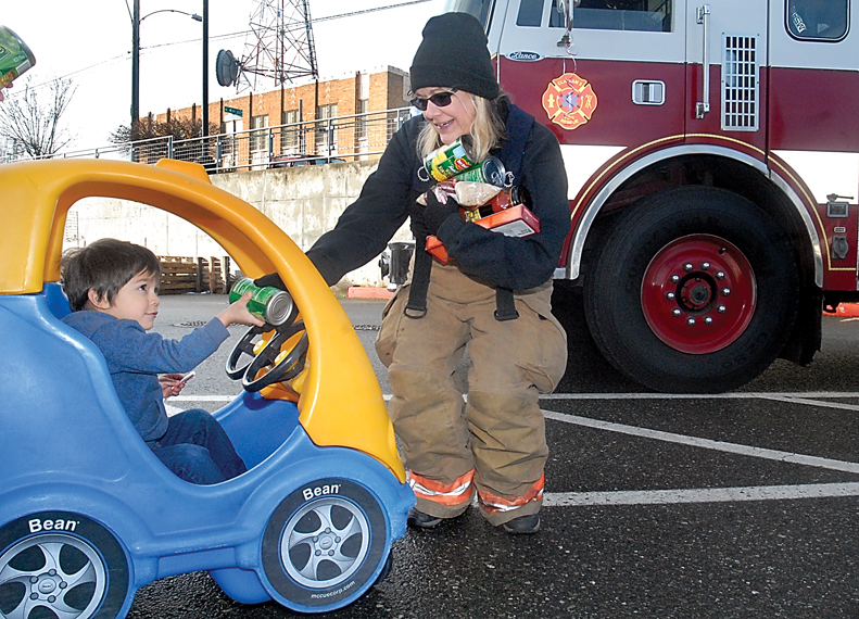 Three-year-old Evan Hernandez passes a can of donated food to Clallam County Fire District 2 emergency medical technician Teresa DeRousie during the “Fill the Fire Engine Food Drive” at the Lincoln Street Safeway grocery store in Port Angeles. Keith Thorpe/Peninsula Daily News