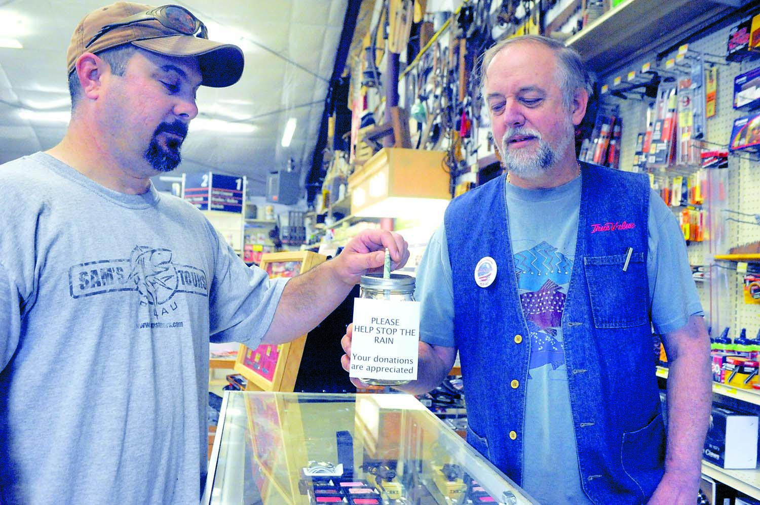 Brian Selk (left) makes a donation to the “Help Stop The Rain” money jar at the Forks True Value Hardware store while store owner Bob Stark looks on. Lonnie Archibald/for Peninsula Daily News