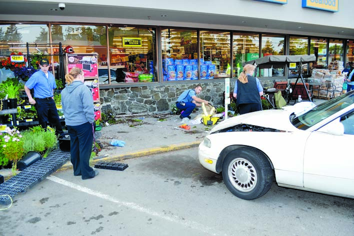 A Jefferson County Sheriff's Office deputy and others looks over the scene after a car ran into a porch swing in front of the QFC grocery store in Port Hadlock on Thursday afternoon. One woman was injured in the crash
