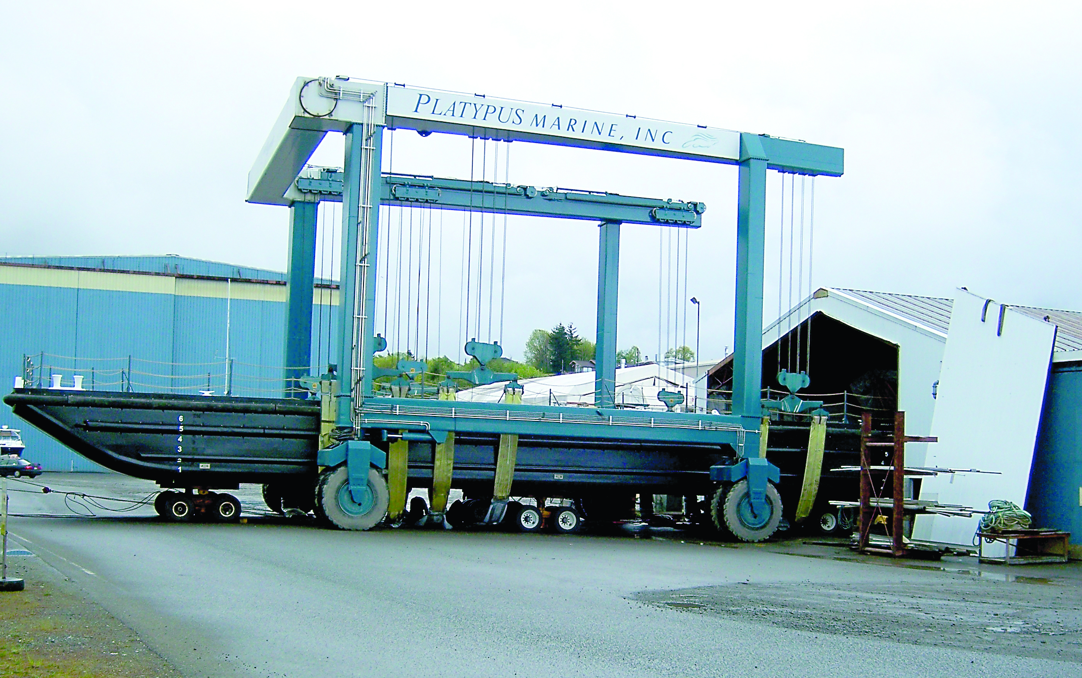 A huge Navy work barge sits in the slings of Platypus Marine Inc.’s TraveLift as it’s carefully maneuvered out of a shop building and into the water.  -- Photo by David G. Sellars/for Peninsula Daily News
