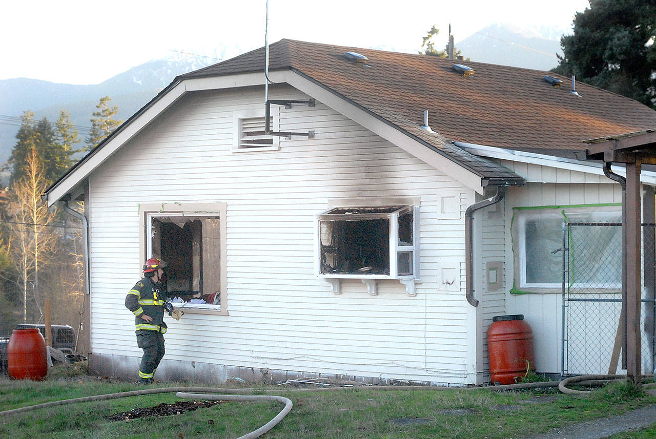 Port Angeles Fire Department Capt. Terry Reid peers through a shattered window at firefighters working inside a house at 802 S. I St., after it was damaged by fire Thursday afternoon. (Keith Thorpe/Peninsula Daily News)